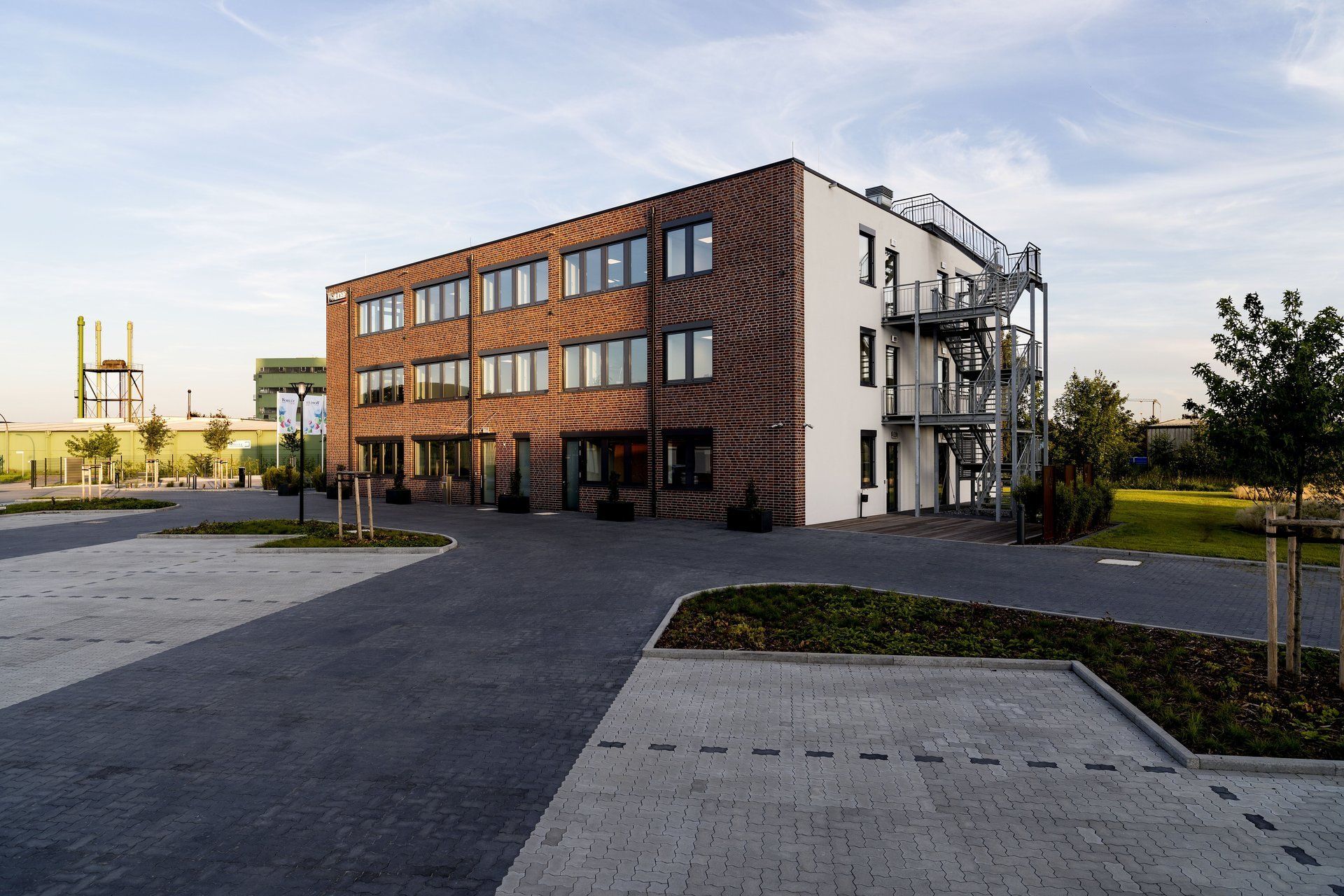 Modernes Backsteinbürogebäude mit großen Fenstern und einem gepflasterten Parkplatz bei Sonnenuntergang