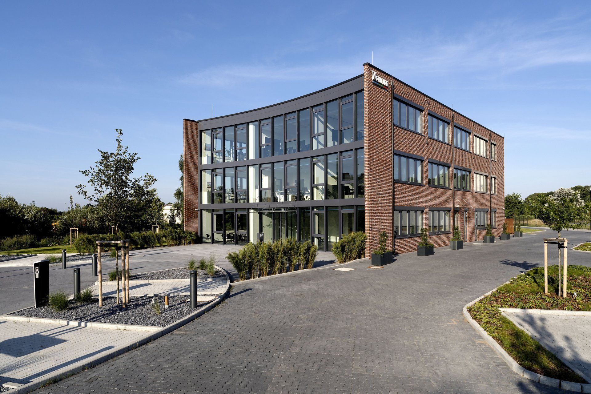 Modernes Bürogebäude aus Backstein und Glas mit geschwungener Fassade und Parkplatz
