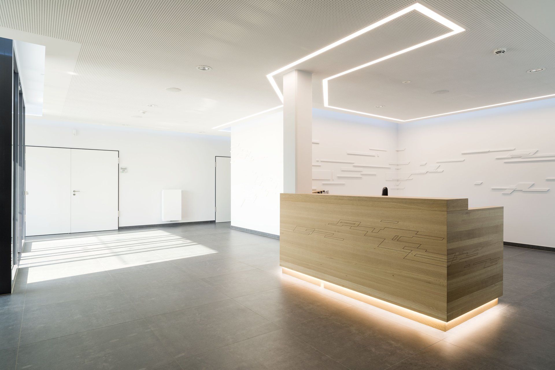 Moderne, minimalistische Bürolobby mit hölzerner Empfangstheke und hellweißen Wänden und Deckenleuchten