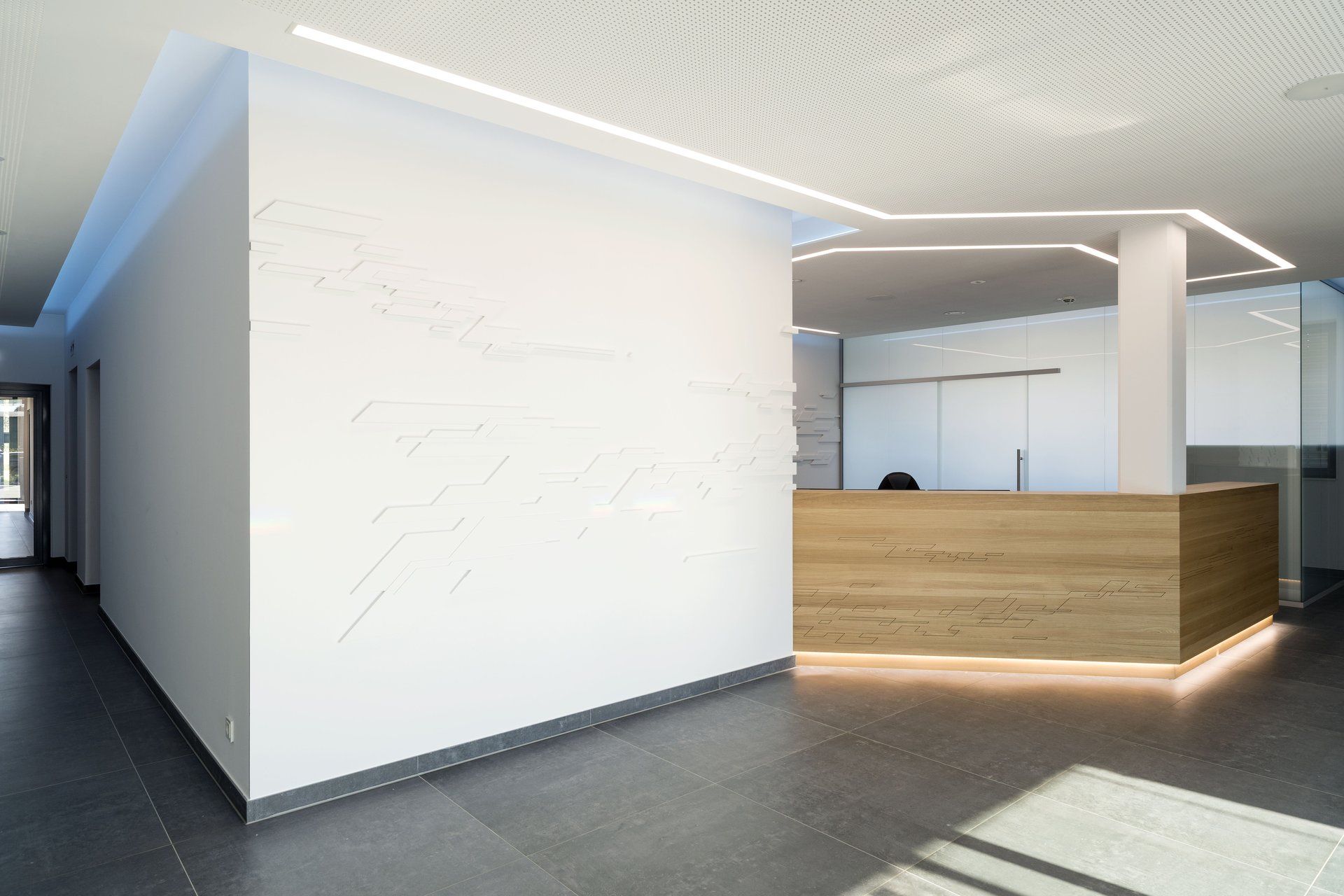 Moderne Bürolobby mit weißen Wänden, grauem Boden und einem Empfangstresen aus Holz mit sanfter Beleuchtung.
