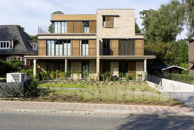 Modernes dreistöckiges Haus mit Balkonen, großen Fenstern und einem Vorgarten zur Straße hin