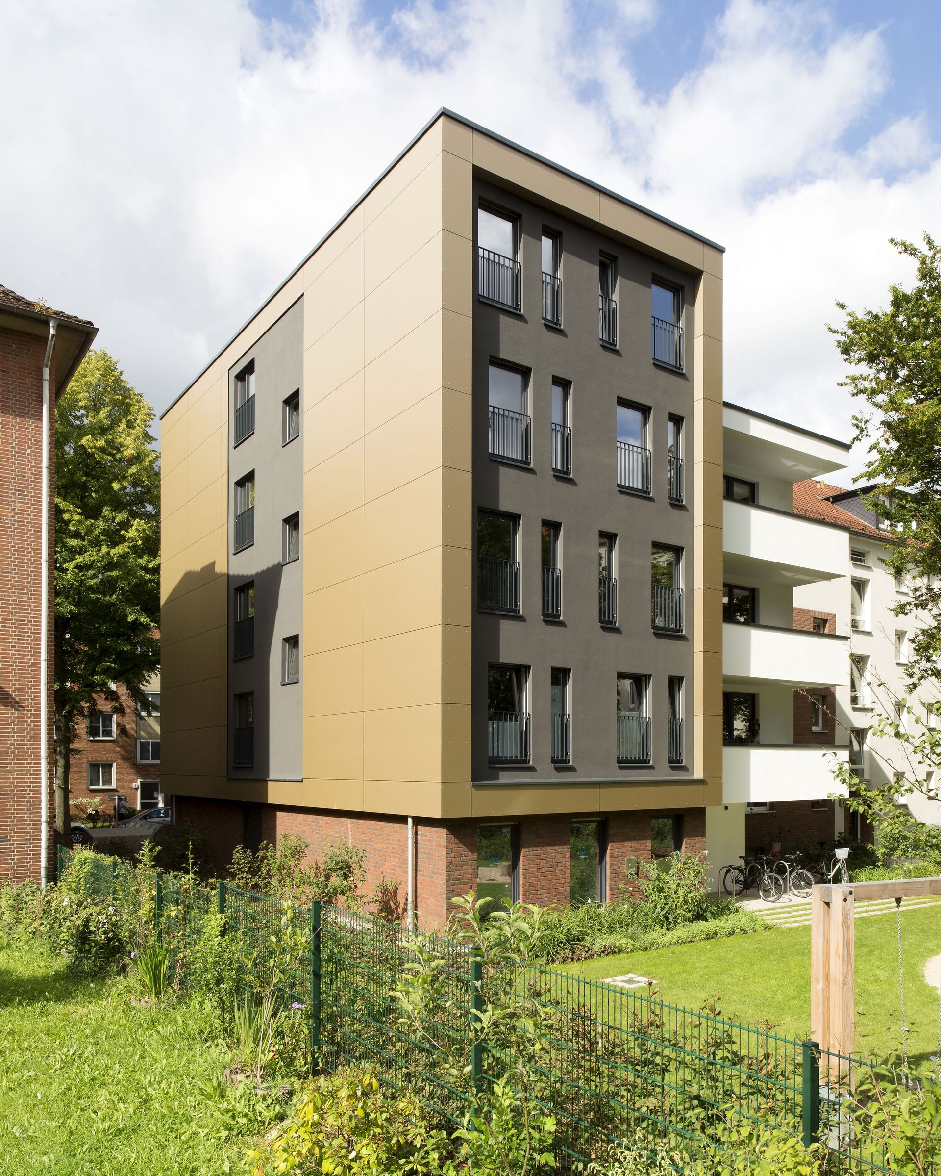 Modernes Mehrfamilienhaus mit beiger und dunkelgrauer Fassade, umgeben von Rasen und Bäumen