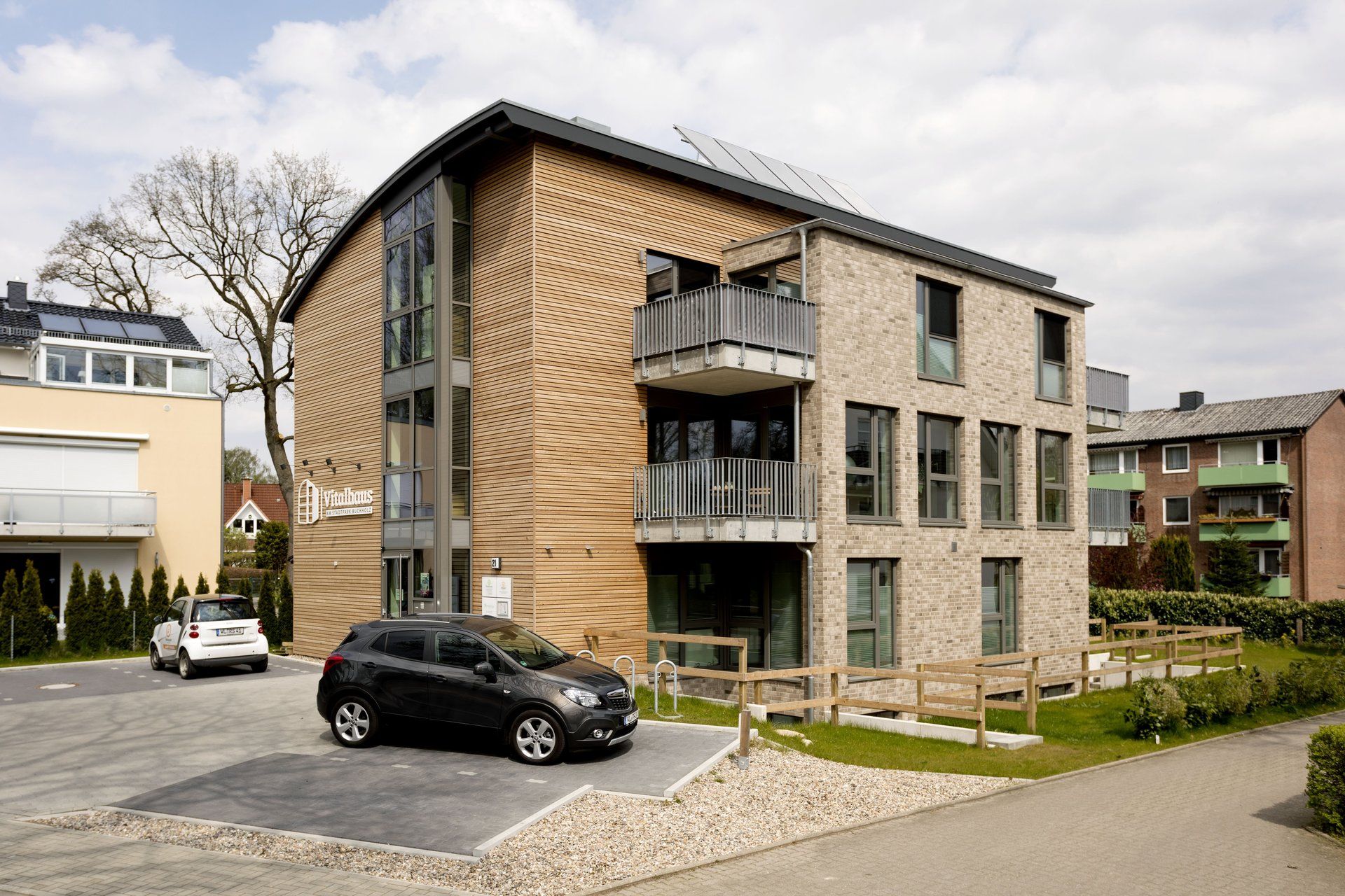 Modernes Wohnhaus mit Balkonen, geparkten Autos und einem begrünten Innenhof an einem bewölkten Tag