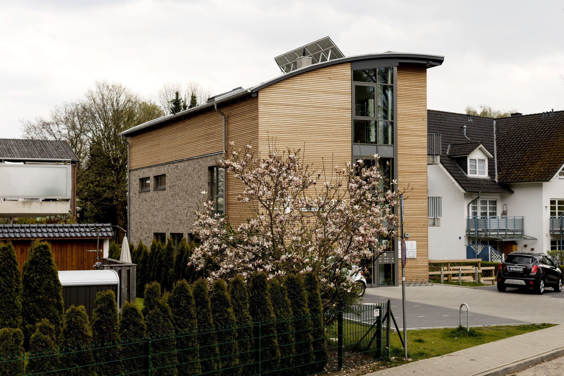 Modernes Haus mit beiger Fassade und großen Fenstern an einer Straße mit geparkten Autos