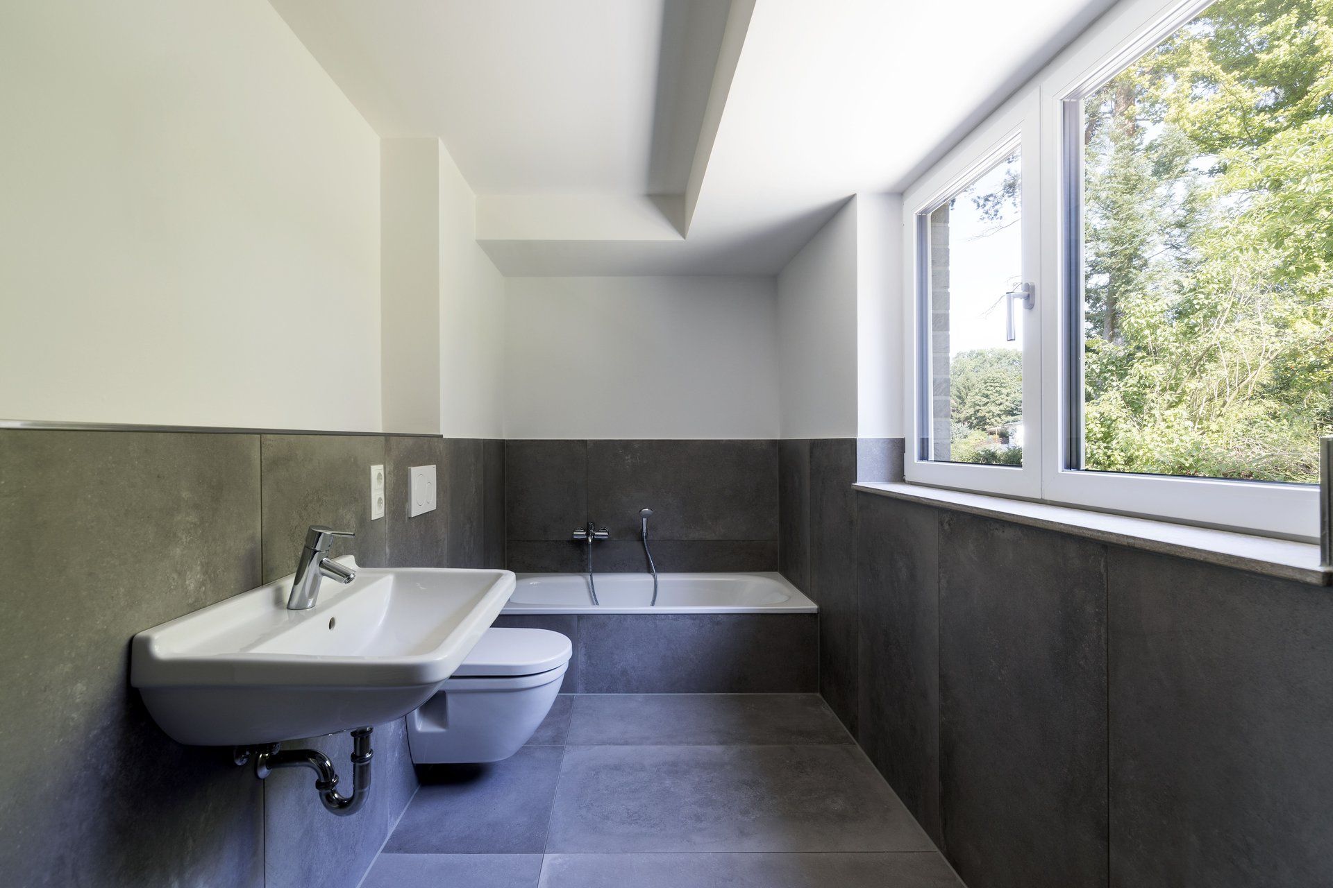 Modernes Badezimmer mit Waschbecken, Toilette, Badewanne und großem Fenster mit Blick ins Grüne