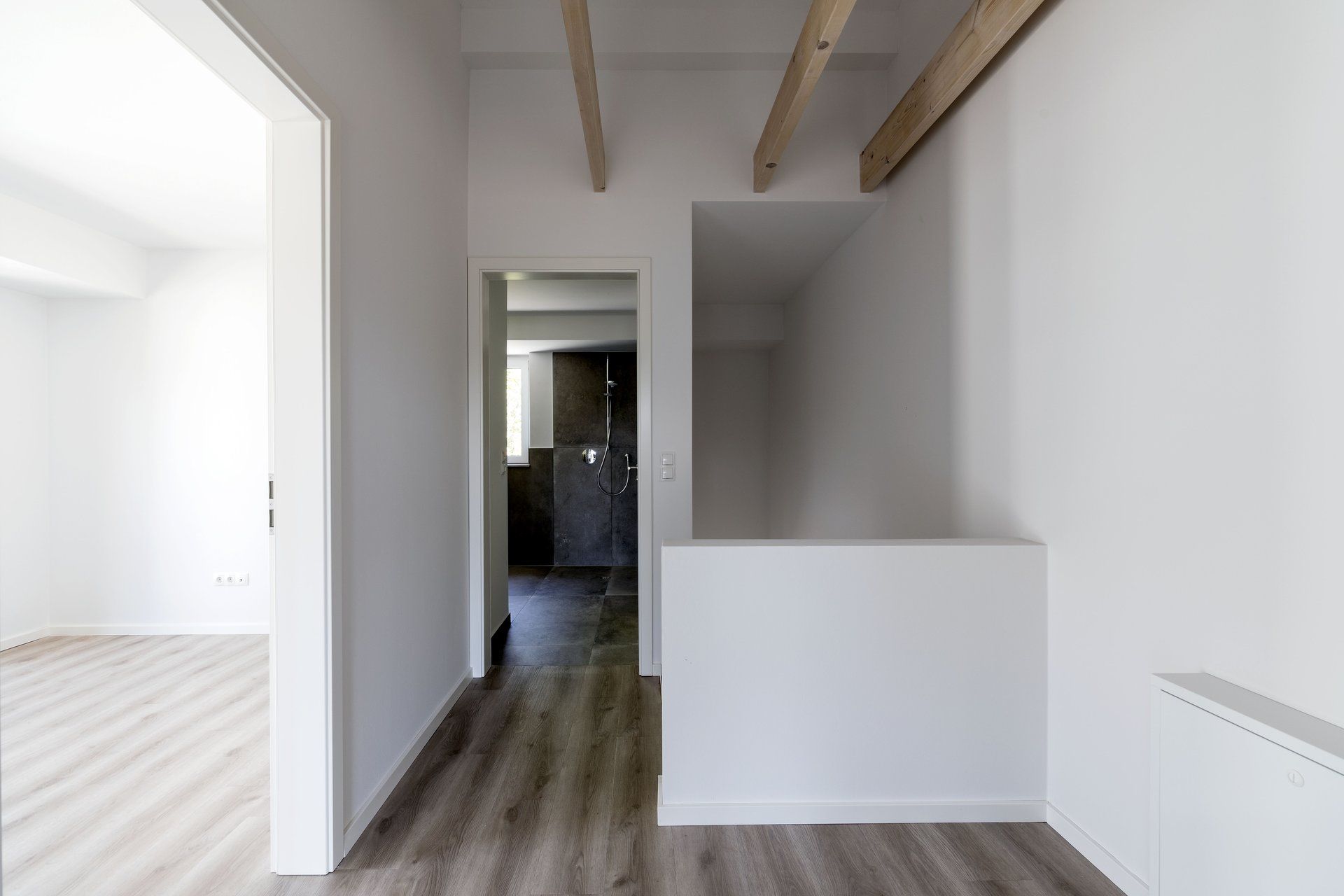 Leerer Flur mit weißen Wänden, Holzböden, freiliegenden Deckenbalken und einer teilweise weißen Trennwand.