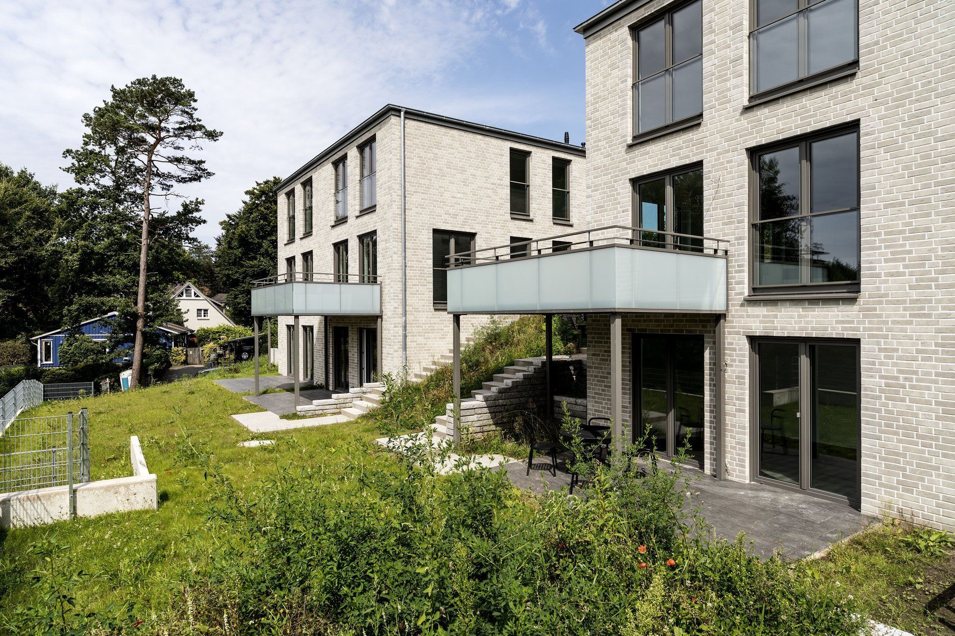 Modernes Apartmentgebäude mit Glasbalkon, Steinfassade und angelegtem Garten an einem sonnigen Tag