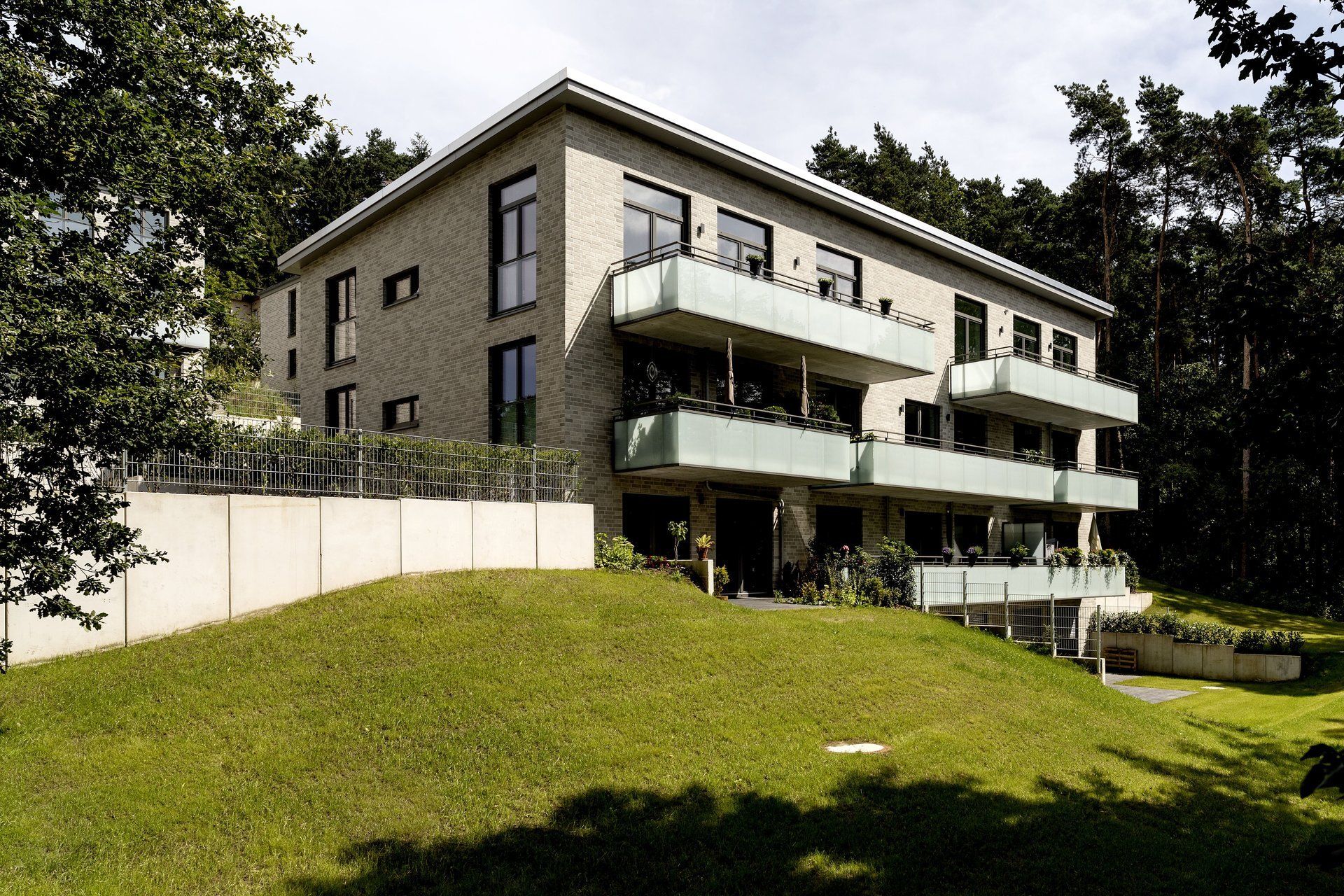 Modernes Mehrfamilienhaus mit Balkonen an einem grasbewachsenen Hang neben Bäumen