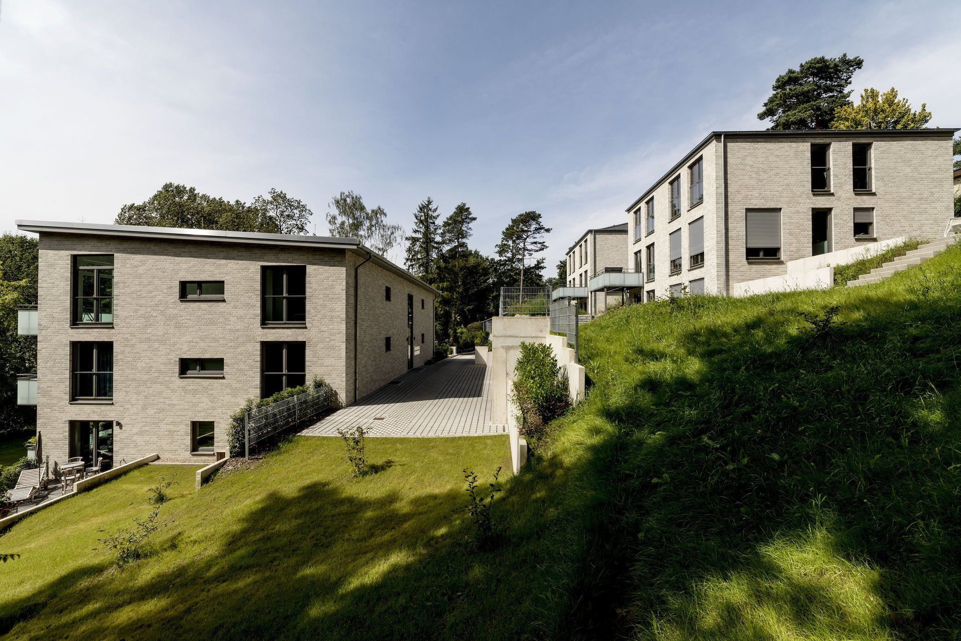 Moderne Apartmentgebäude an einem grasbewachsenen Hang mit gepflastertem Gehweg und Bäumen unter klarem Himmel