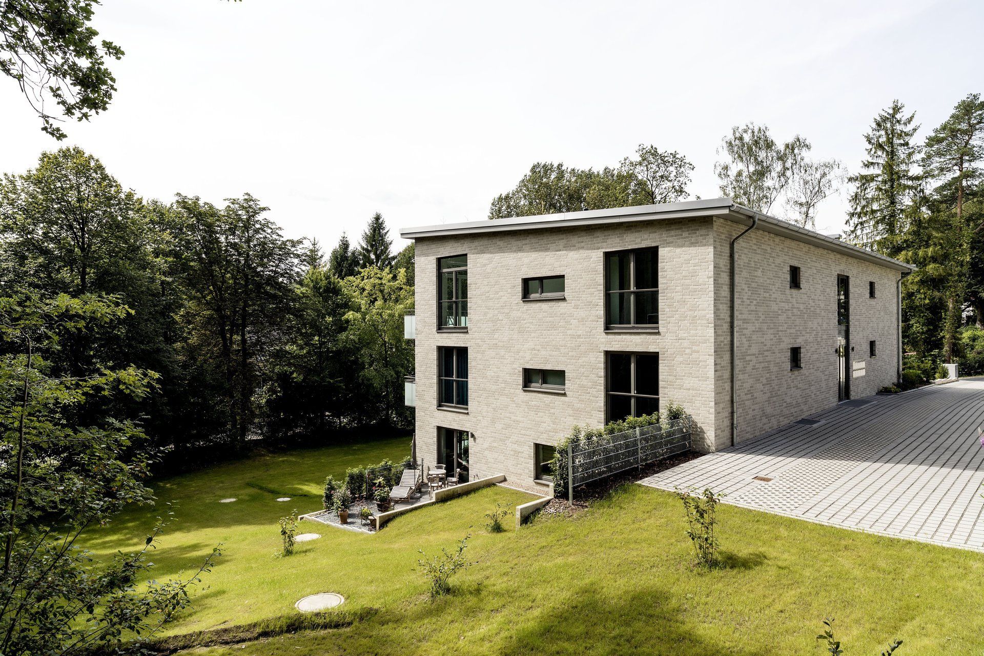 Modernes beigefarbenes Haus mit Steinfassade, umgeben von grünem Rasen und Bäumen an einem sonnigen Tag