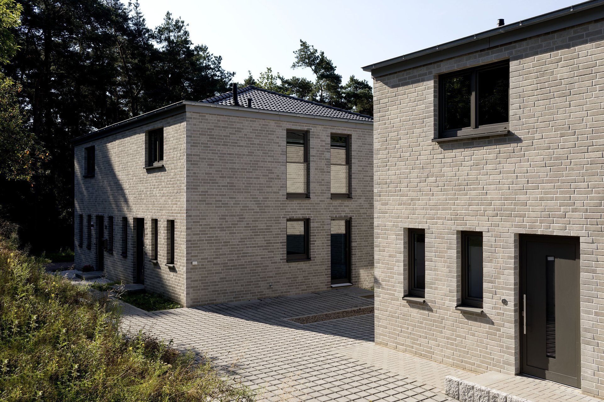 Moderne beige Backsteingebäude mit schwarzen Fenstern und einem gepflasterten Innenhof unter Bäumen