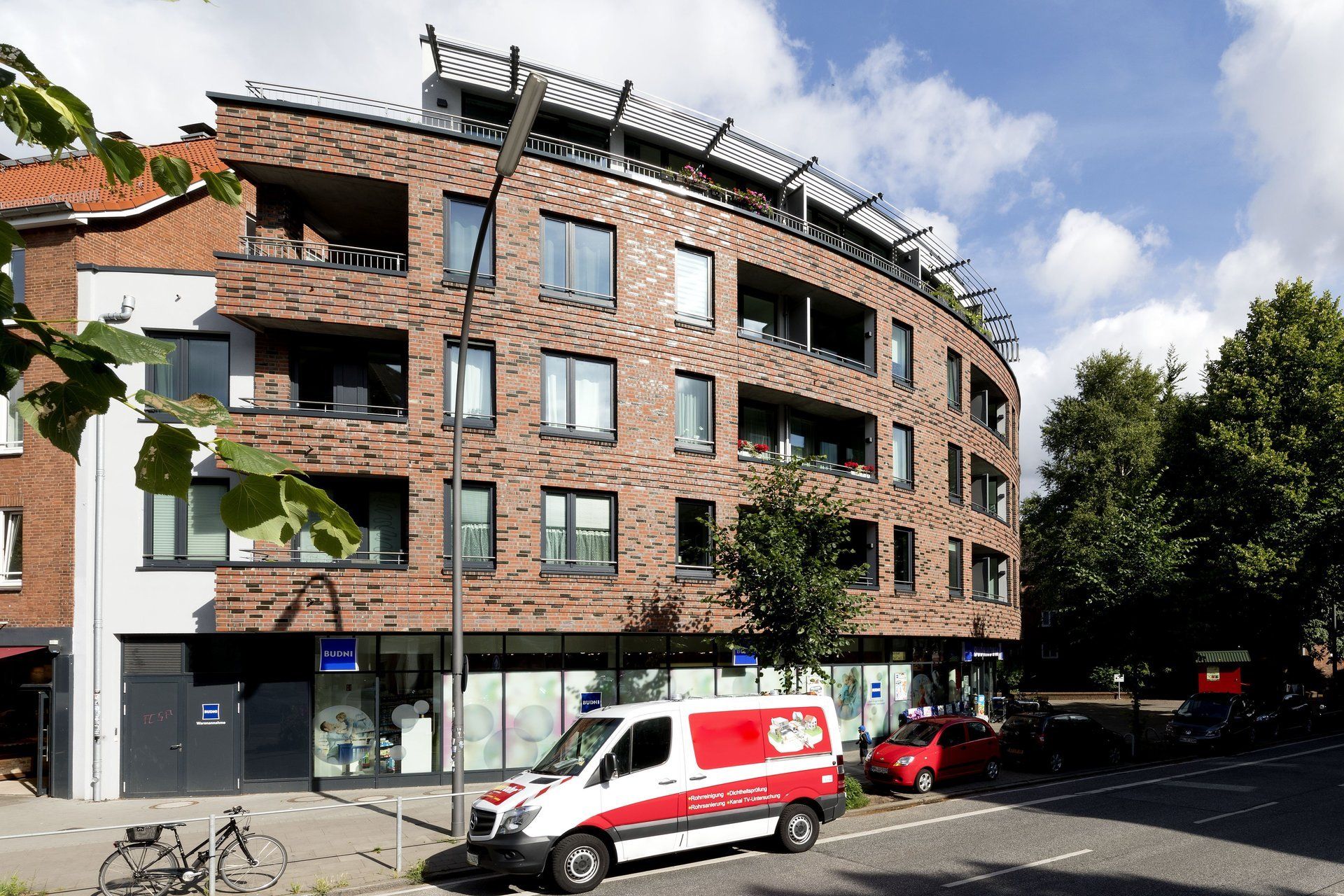 Modernes Backstein-Mehrfamilienhaus in einer sonnigen Straße mit geparkten Lieferwagen und Autos