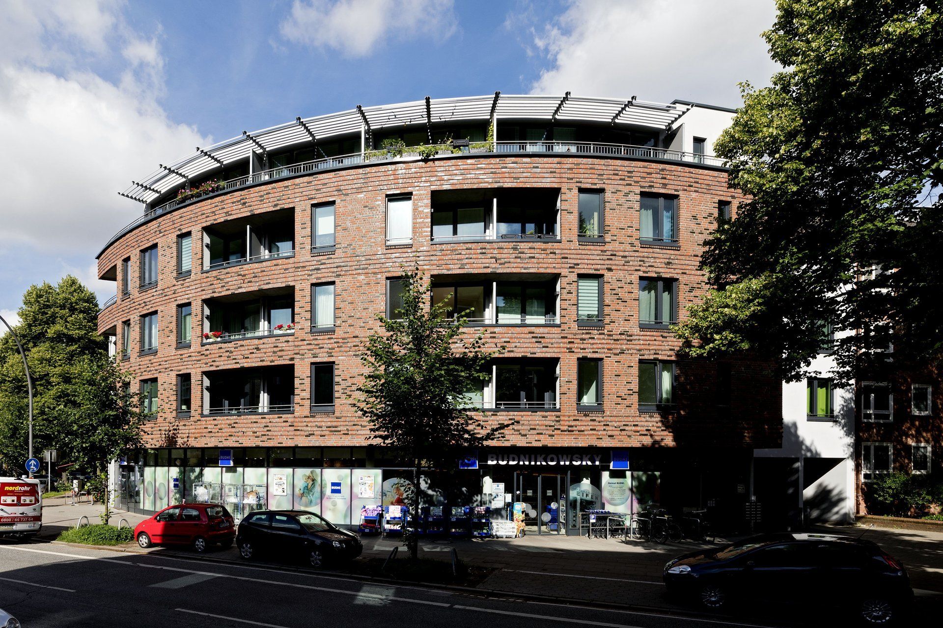Geschwungenes Backstein-Wohnhaus mit Geschäften im Erdgeschoss an einer sonnigen Stadtstraße