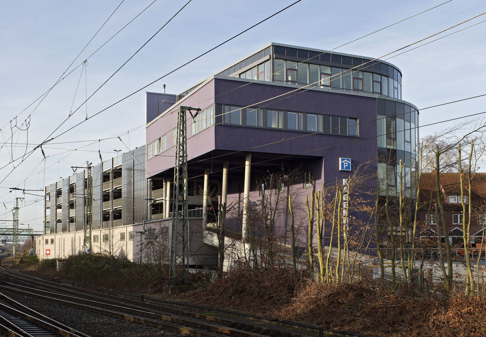 Modernes mehrstöckiges Gebäude neben Bahngleisen unter einem blassen Himmel