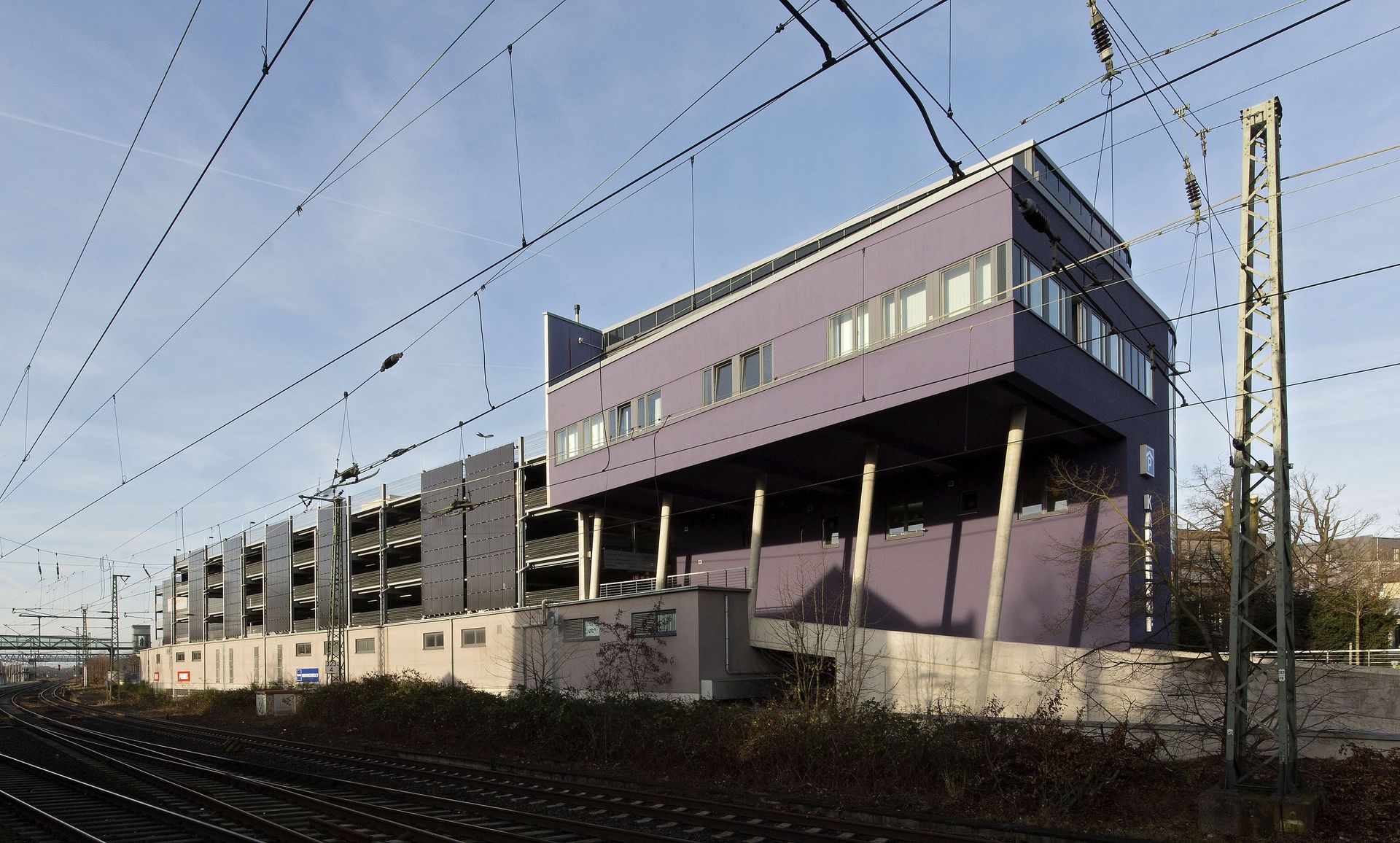 Lila Bahnhofsgebäude neben Bahngleisen unter klarem Himmel