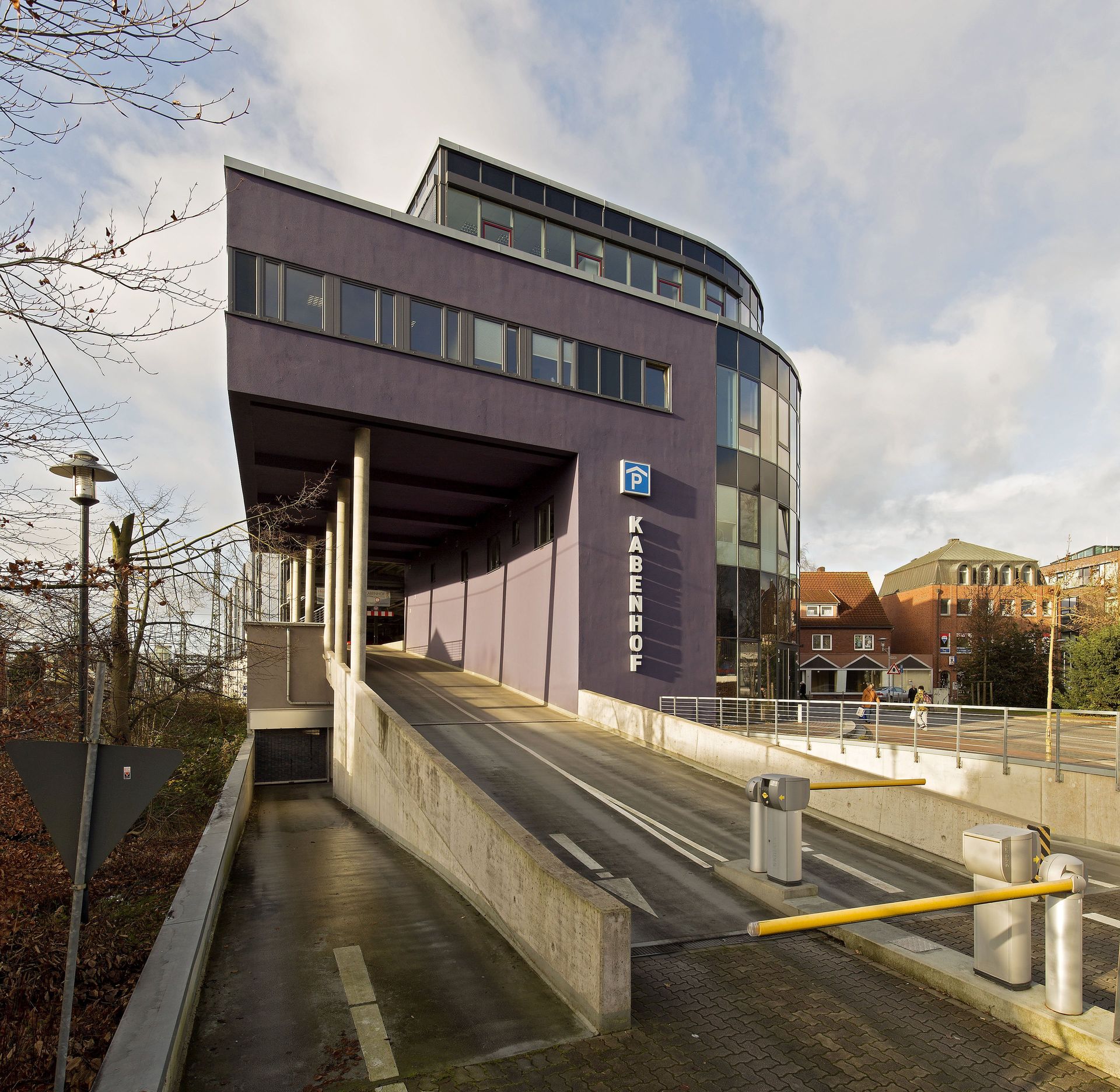 Modernes, lilafarbenes Bahnhofsgebäude mit schräger Rampe und Treppe unter einem bewölkten Himmel