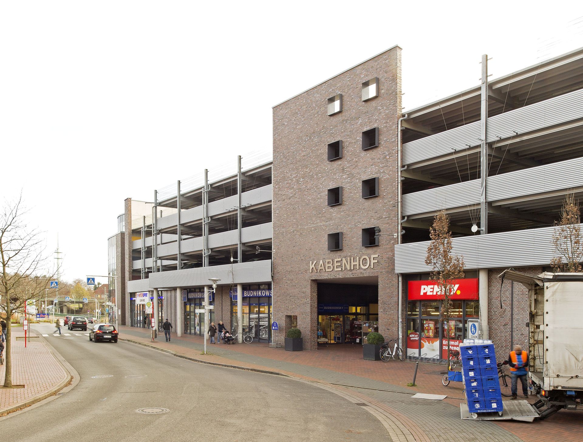 Mehrstöckiges Parkhaus an einer kurvigen Straße mit Ladenfronten und Schildern im Erdgeschoss