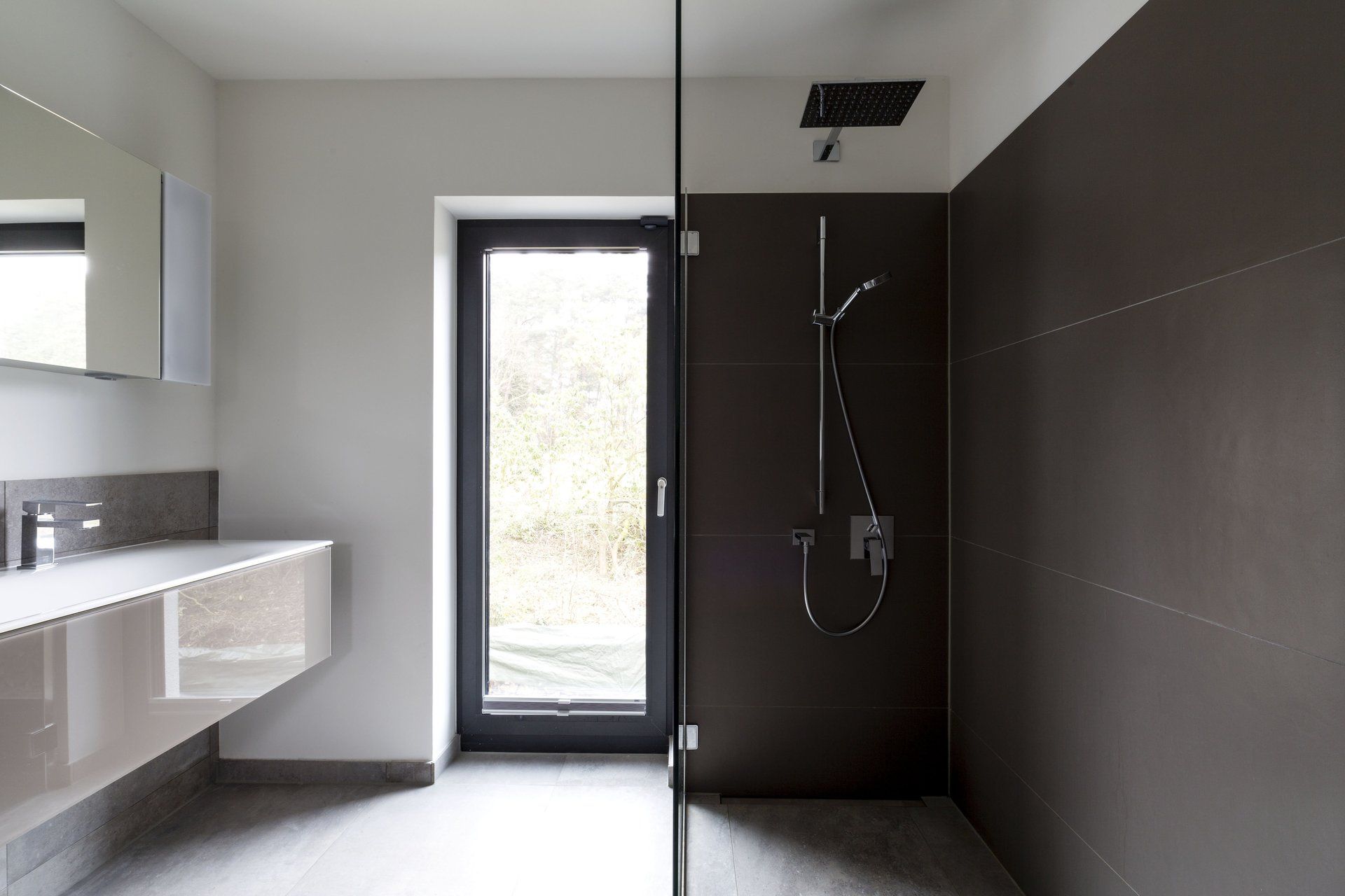 Modernes Badezimmer mit ebenerdiger Dusche, weißem Waschtisch und Glastür mit dunkel gefliester Akzentwand