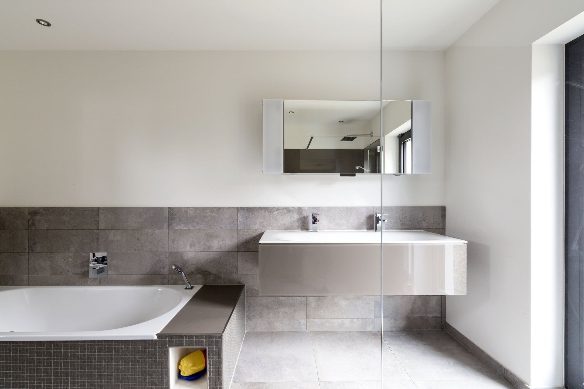 Modernes Badezimmer mit freistehender Badewanne, schwebendem Waschbecken, Spiegel und grauen Fliesenakzenten