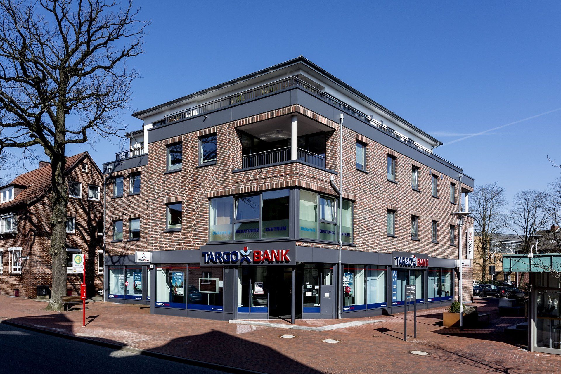 Eckgebäude mit Backsteinfassade und blauen Markisen an einer sonnigen Straßenecke