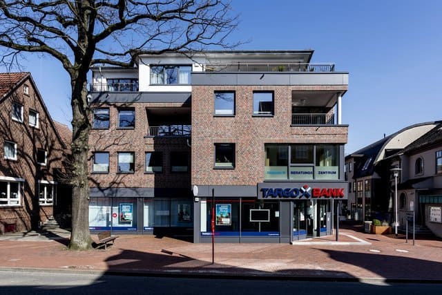 Gemischt genutztes Backsteingebäude mit Ladenlokalen im Erdgeschoss und Wohnungen darüber an einer sonnigen Straßenecke
