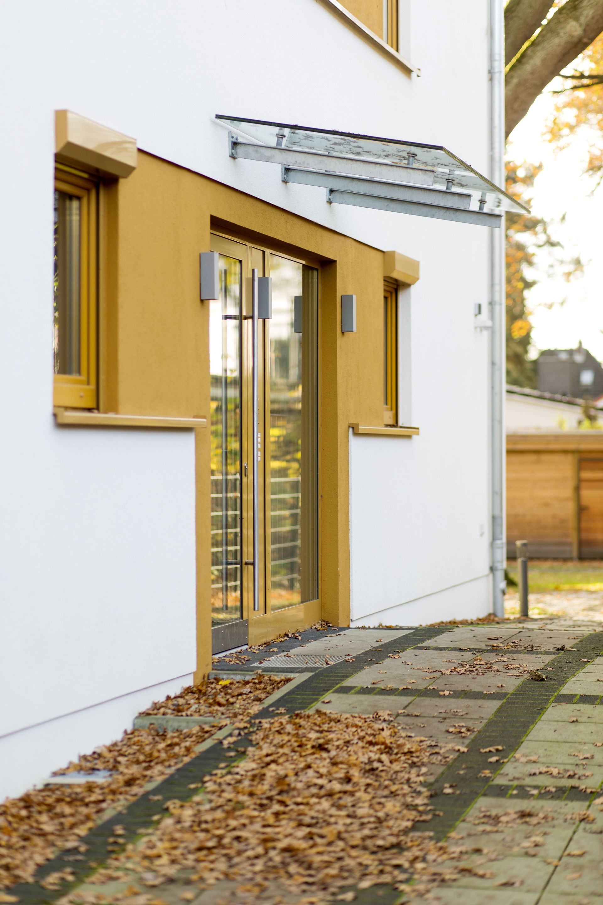 Weißes Haus mit senfgelben Fensterläden, Glastüren und einem mit Laub bedeckten Steinweg