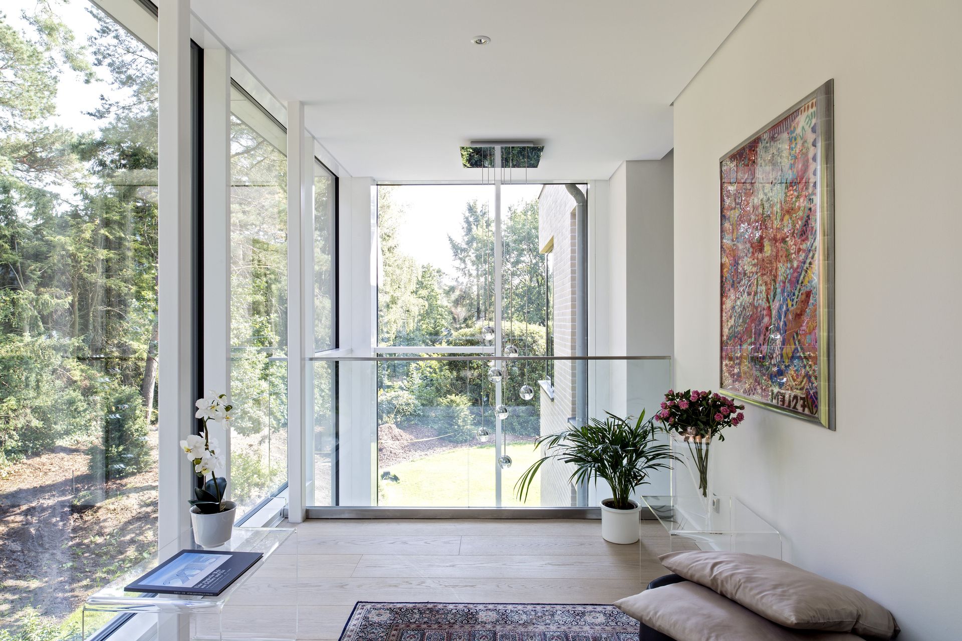 Helles, minimalistisches Wohnzimmer mit großen Fenstern, einem farbenfrohen Wandgemälde und einer Blumenvase.