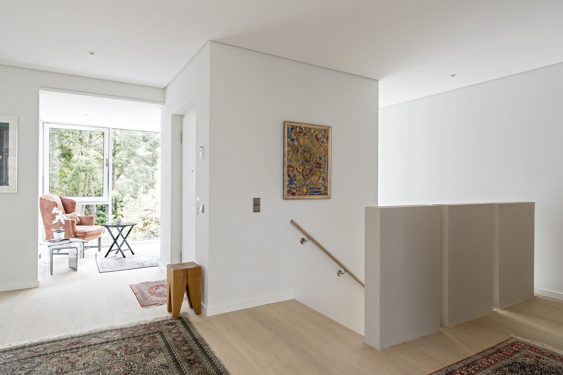 Heller Flur mit Treppe, Wandbildern und einer offenen Tür zu einer sonnigen Terrasse und einem Garten
