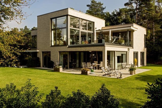 Modernes zweistöckiges weißes Haus mit großen Glasfenstern und grünem Rasen, Blick vom Hinterhof