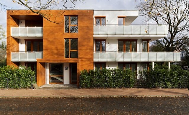 Modernes Wohngebäude mit orangefarbener Mittelfassade, weißen Balkonen und Begrünung am Sockel