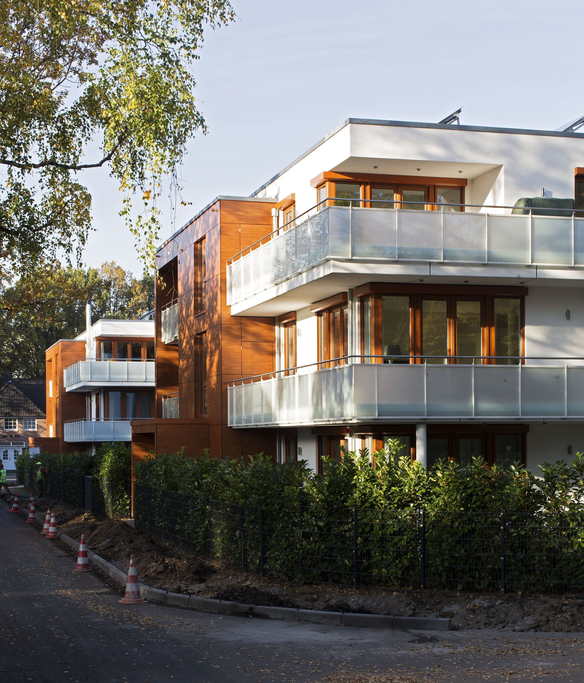 Moderne Wohnhäuser mit Glasbalkonen an einer baumbestandenen Straße bei Tageslicht