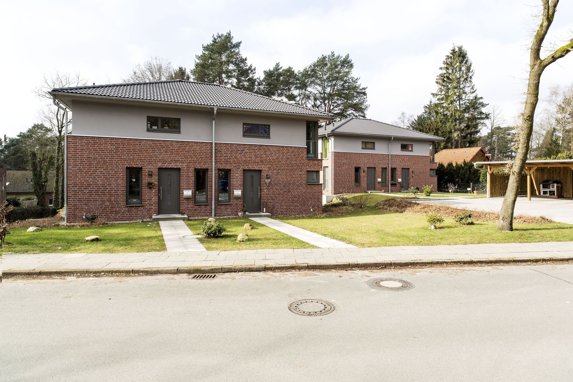 Backstein-Mehrfamilienhaus mit weißem Obergeschoss, Bäumen und einem Bürgersteig entlang der Straße