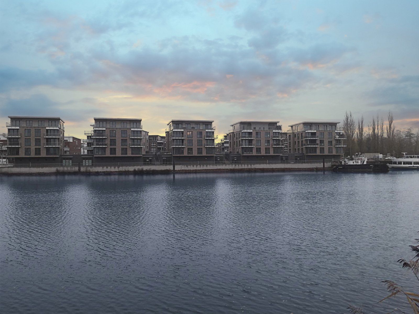 Moderne Apartmentgebäude an einer ruhigen Uferpromenade in der Abenddämmerung unter einem bewölkten Himmel