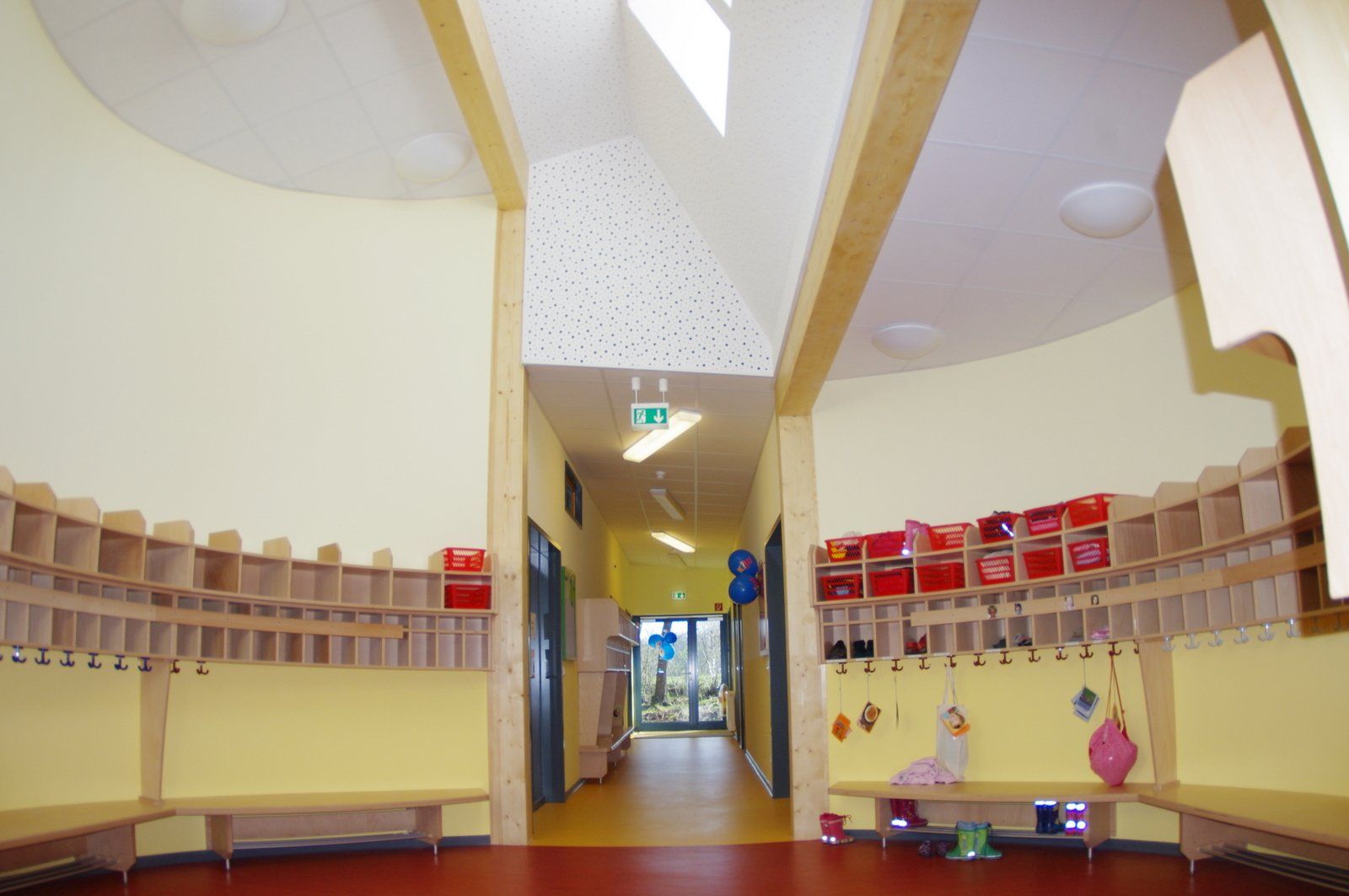 Leerer Flur vor einem Kindergartenraum mit Holzfächern, niedrigen Regalen und hellen Oberlichtern.