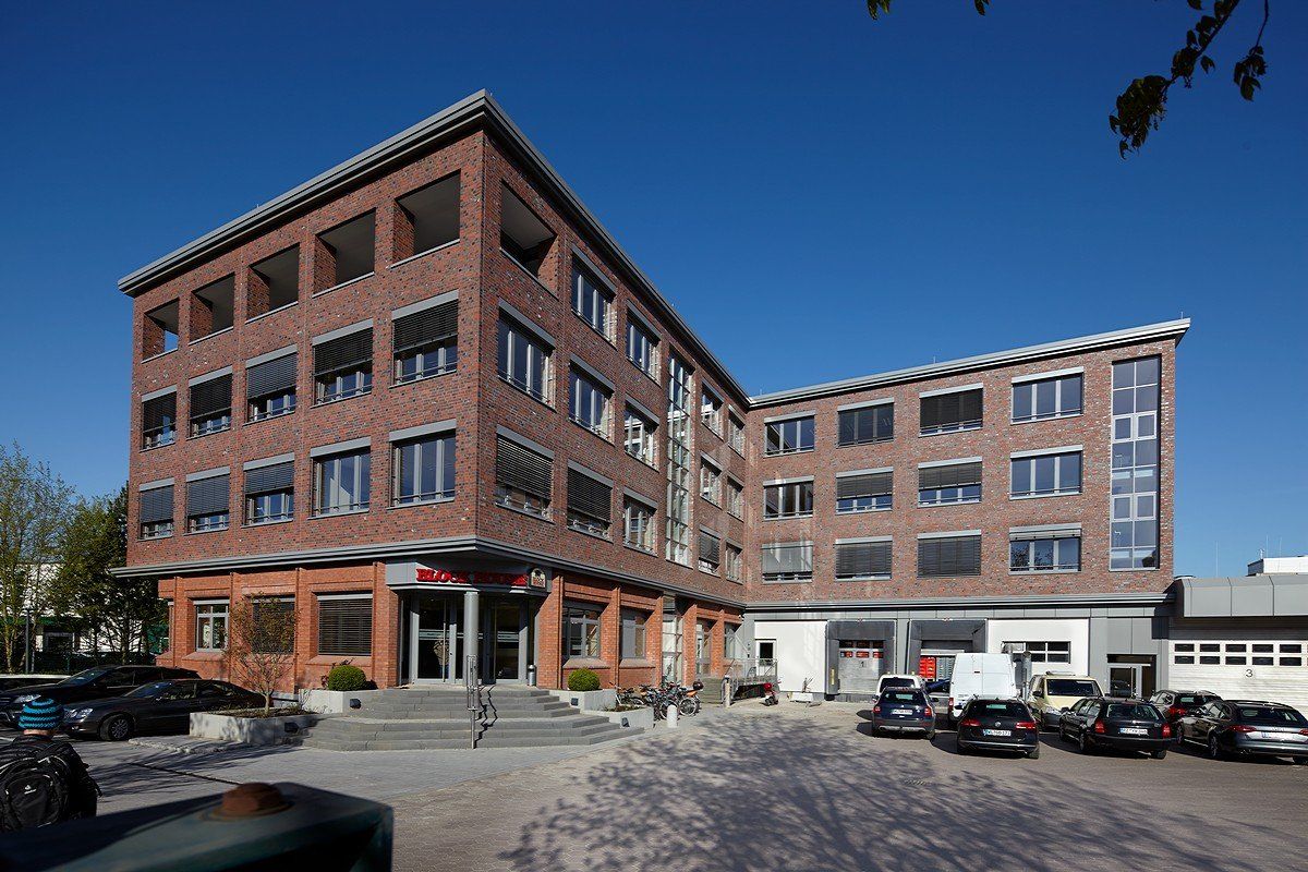 Backsteinbürogebäude mit geparkten Autos auf einem sonnigen Parkplatz unter klarem, blauem Himmel