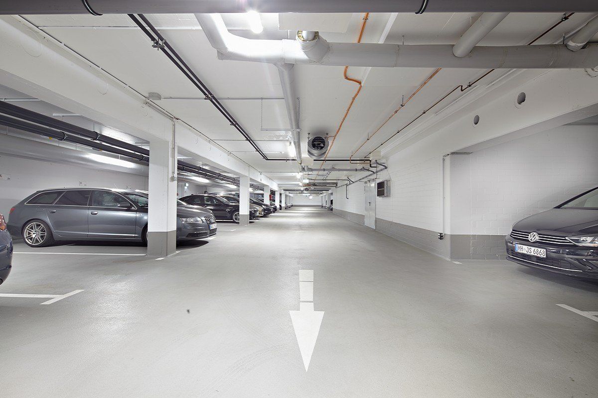 Tiefgarage mit auf beiden Seiten geparkten Autos und einem weißen Richtungspfeil auf dem Boden.