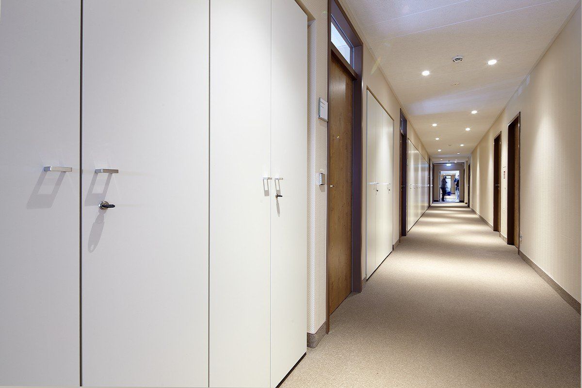 Langer Hotelflur mit beigefarbenem Teppichboden, weißen Türen und Deckeneinbauleuchten