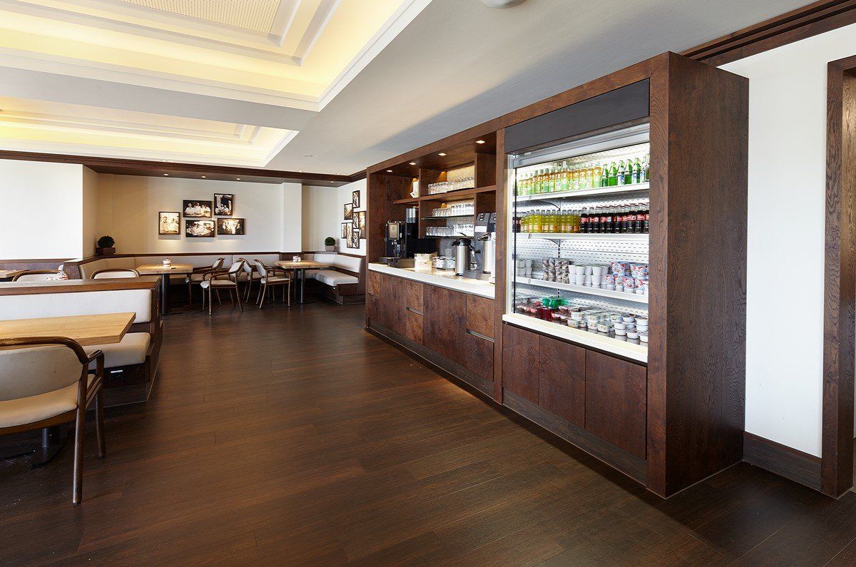 Moderner Restaurant-Speisesaal mit dunklem Holzboden, Sitznischen und einem Barbereich mit beleuchteten Regalen.