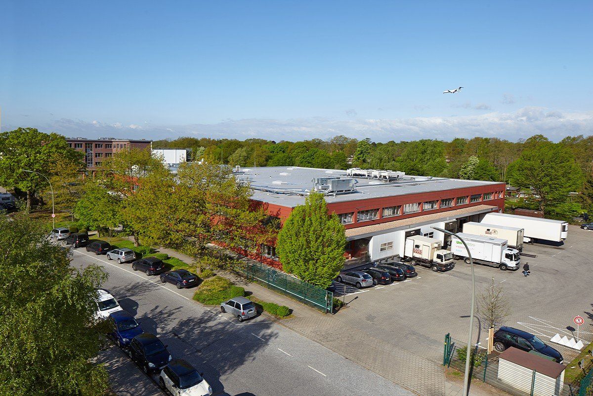 Industriehalle mit Lastwagen auf einem von Bäumen gesäumten Parkplatz an einem sonnigen Tag
