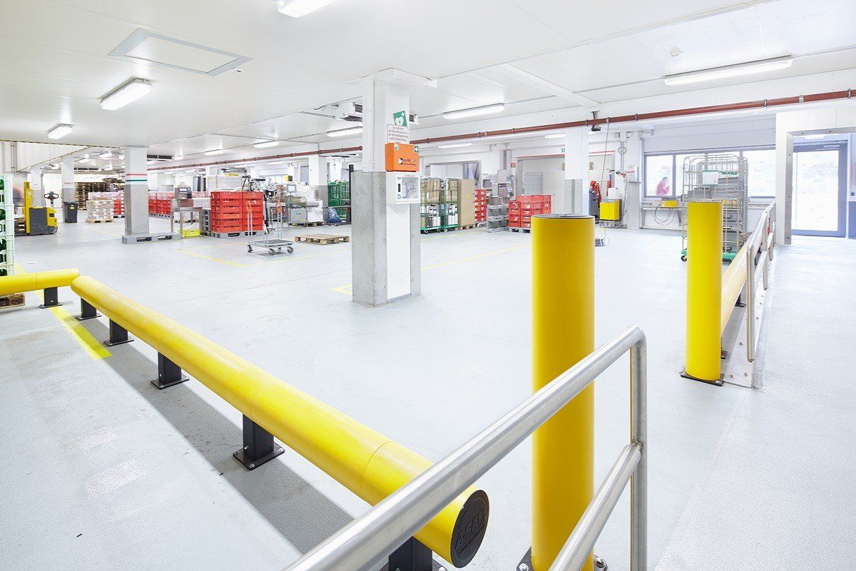 Helles Industriehalleninterieur mit gelben Sicherheitsgeländern und weißen Böden unter Leuchtstoffröhren