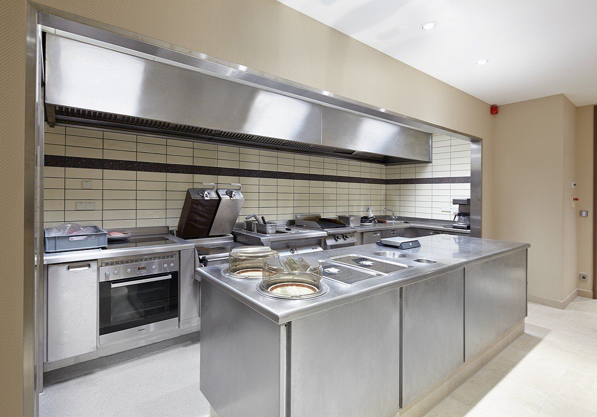 Moderne Buffettheke aus Edelstahl mit Speisenbehältern und großer Dunstabzugshaube in einer gewerblichen Küche