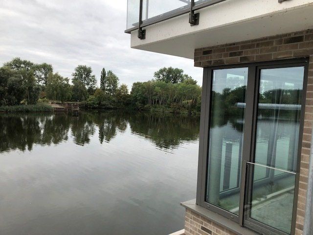 Balkon mit Blick auf einen ruhigen See, in dessen Wasser sich Bäume spiegeln