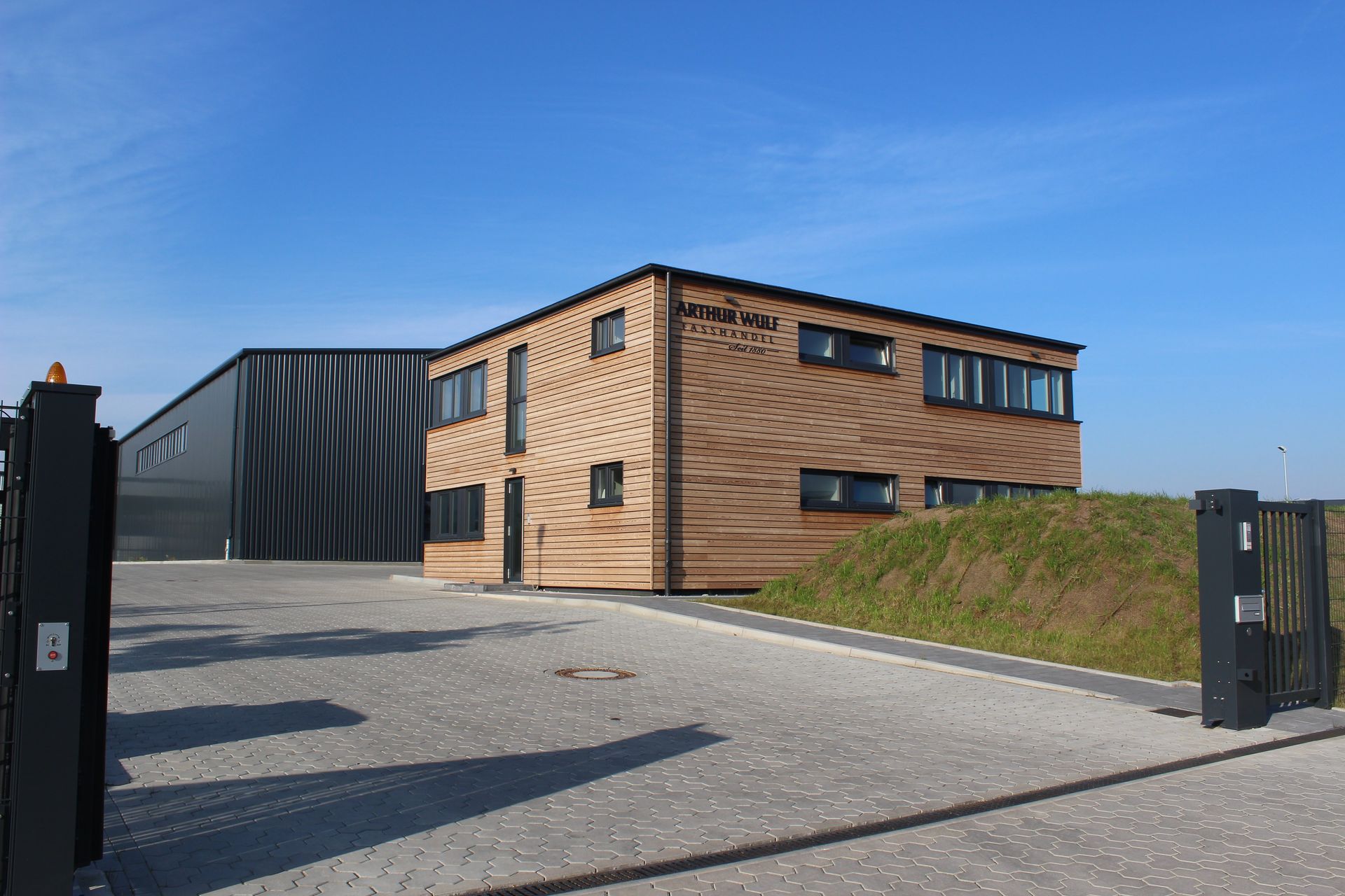 Modernes Backsteingebäude mit einem dunklen Metallanbau, Kiesauffahrt und blauem Himmel.