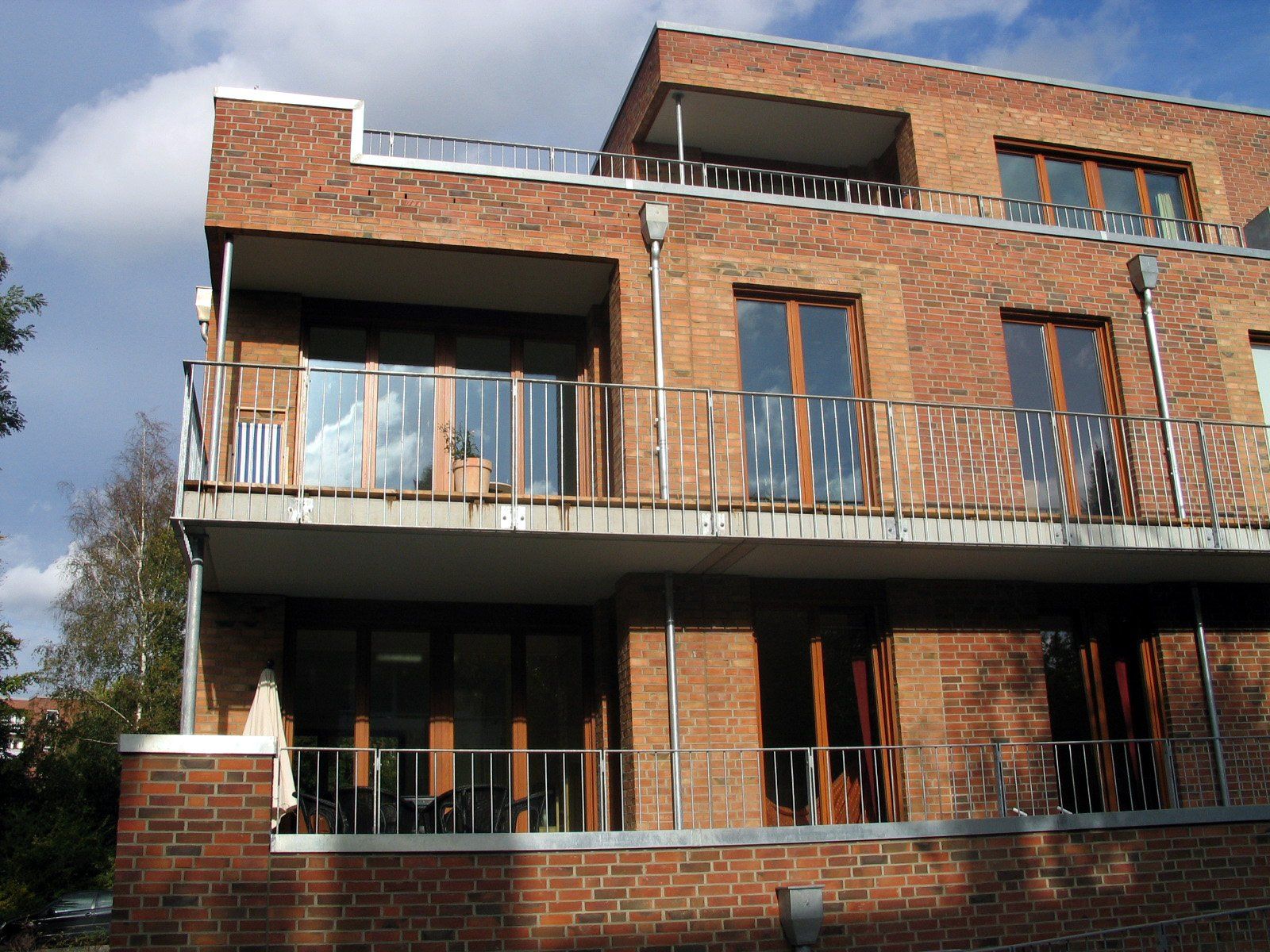Backstein-Wohnhaus mit Balkonen und großen Fenstern unter einem teilweise bewölkten Himmel