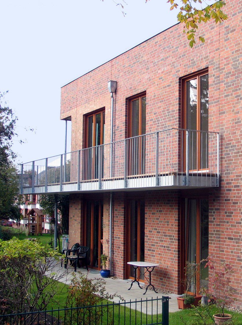 Backsteingebäude mit Balkon und Terrassentischen neben einem Gartenweg