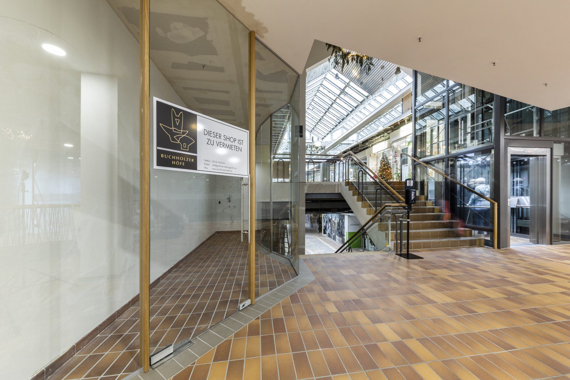 Moderne Lobby mit Glaswänden, Treppenhaus, Aufzug und Holzbodenoptik.