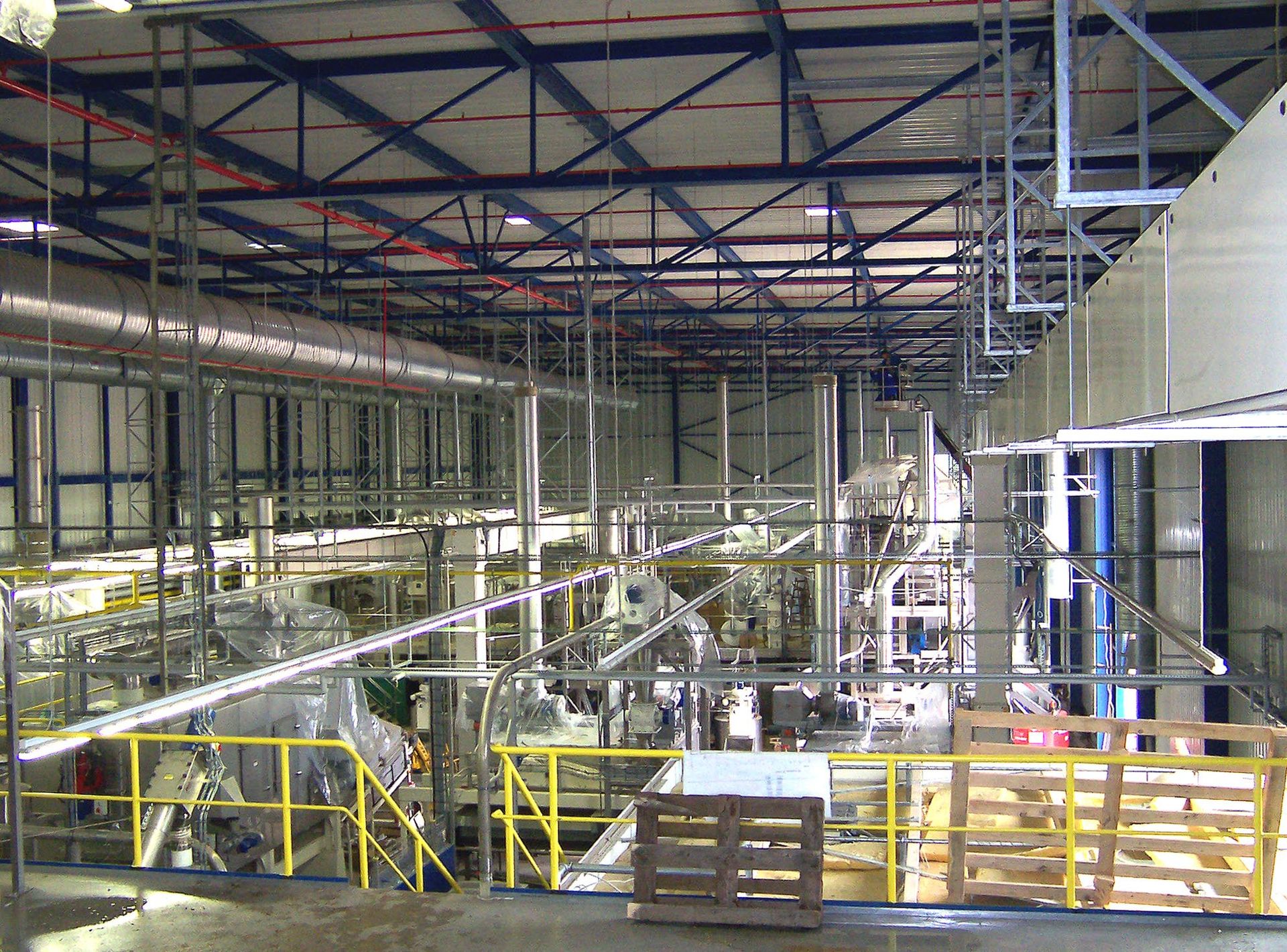 Industriehalleninterieur mit Stahlträgern, Maschinen und gelben Sicherheitsgeländern