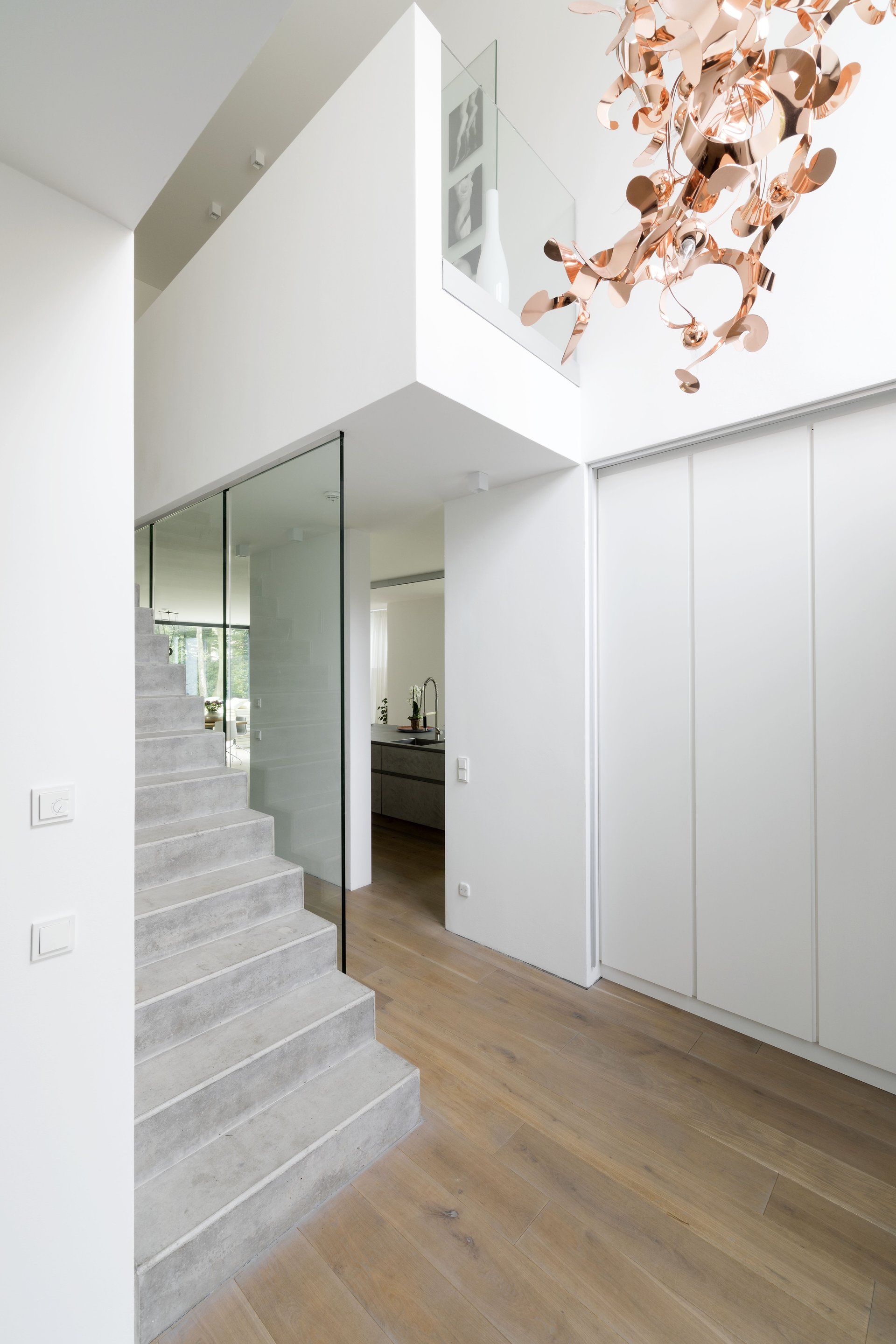 Modernes Treppenhaus mit Holzböden, weißen Wänden, Spiegelpaneelen und einer hängenden Kupferblattskulptur.