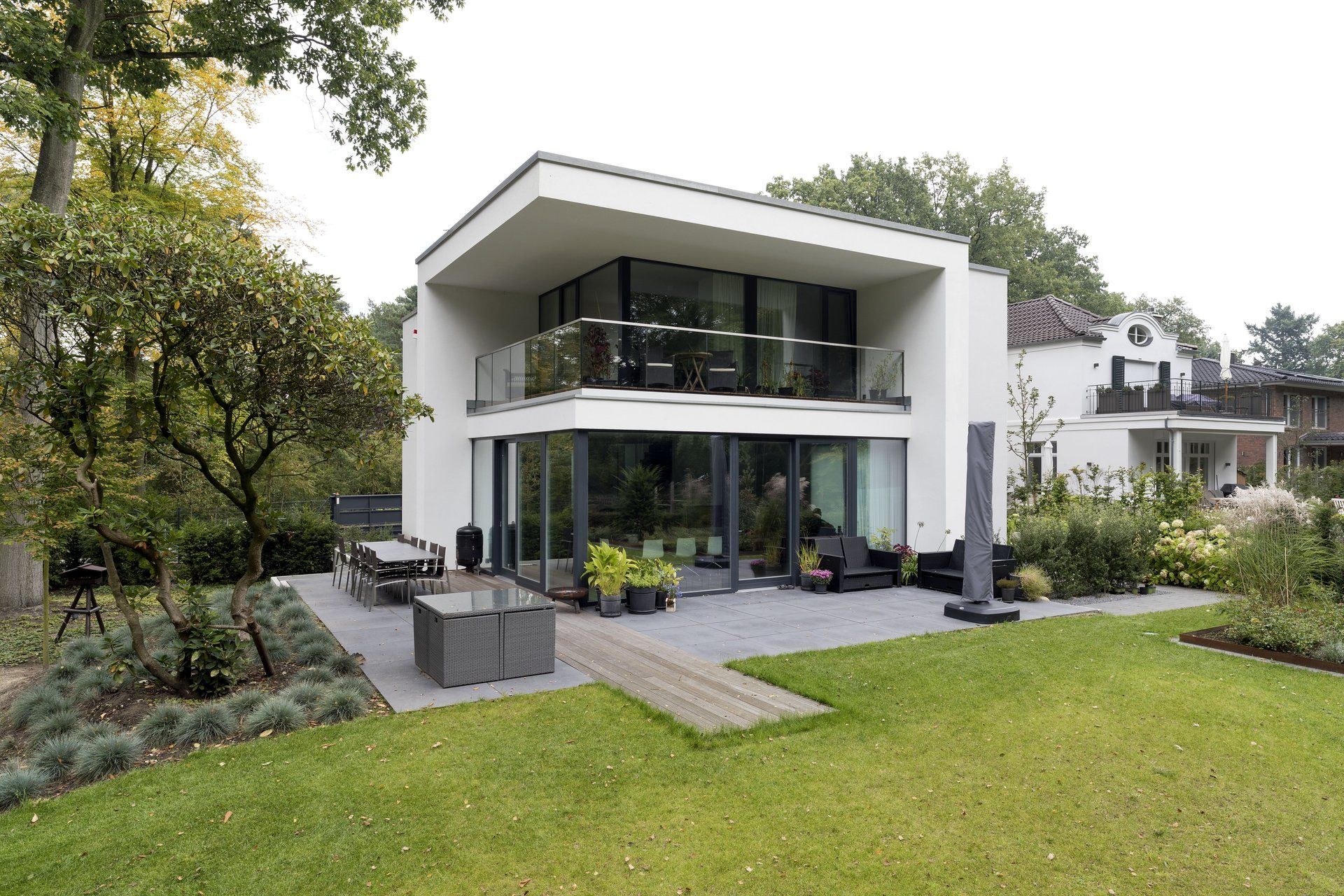 Modernes zweistöckiges weißes Haus mit großer Glasterrasse und angelegtem Garten
