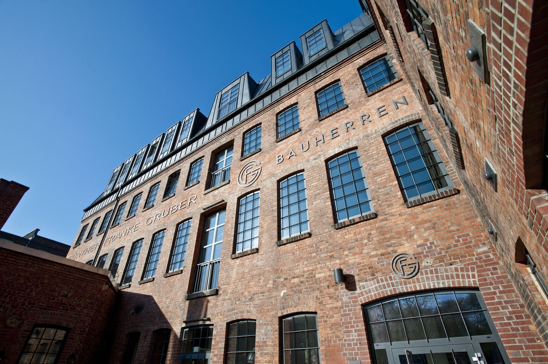Ansicht von unten auf ein Backsteingebäude mit vielen Fenstern vor blauem Himmel